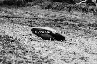 Monochrome 1967 photograph of a small Flying Saucer apparently landed in a field. A vehicle can be seen in the distance. Photo copyright 2008 John Keeling